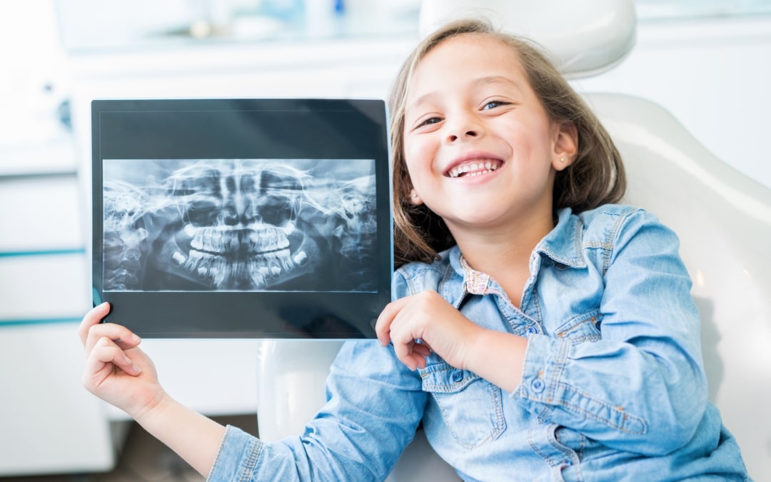 Young girl is sitting in the dental chair holding an X-ray of her teeth.